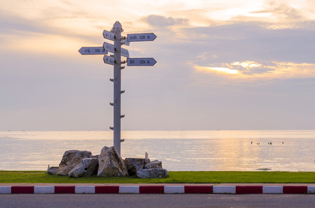 An image of arrow sign pole lacated on the road near the sea in sunset time