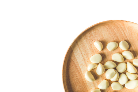 Peeled Garlic cloves on round wooden plate isolated at corner on white backgroundの写真素材