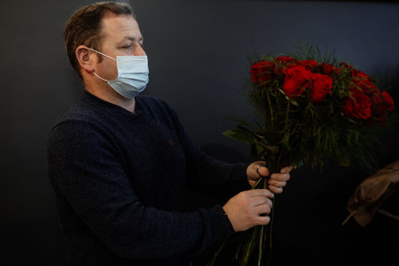 Happy caucasian florist making bouquets of red and pink roses for Valentine's day. Concept of human emotions, facial expression, love, and hard work in this pandemic times.の写真素材