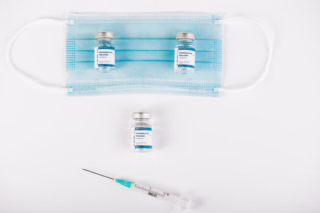 Zenith shot of Vaccine vials, mask and syringe with white background. Smile medical concept. Copy space.の写真素材