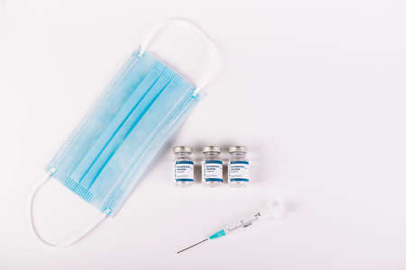 Zenith shot of Vaccine vials, mask and syringe with white background. Medical still life concept....