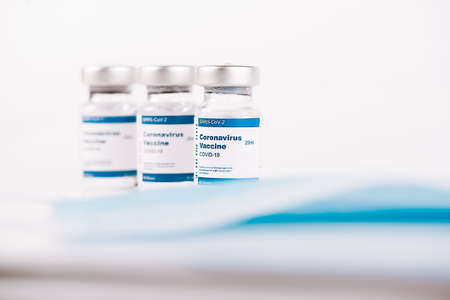three Covid-19 vaccine vials and blue mask with white background and a syringe to inject medical...