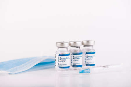 three Covid-19 vaccine vials and blue mask with white background and a syringe to inject medical...