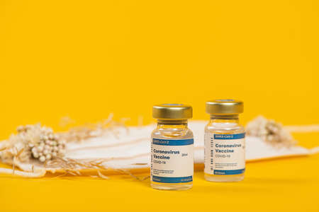 Three Coronavirus Vials And Syringe With Medical Face Mask With Pink Flowers On It. Creative concept of seasonal flu, allergies or coronavirus.の写真素材