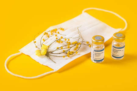Three Coronavirus Vials And Syringe With Medical Face Mask With Pink Flowers On It. Creative concept of seasonal flu, allergies or coronavirus.の写真素材