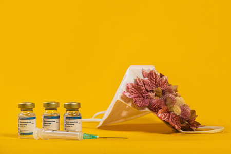 Three Coronavirus Vials And Syringe With Medical Face Mask With Pink Flowers On It. Creative concept...
