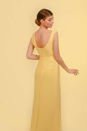 Medium shot of beautiful stylish fashion girl in yellow dress looking down. Isolated on yellow background. Design copy space.の写真素材