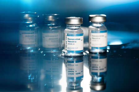 Two Covid-19 vaccine vials on blue background and back light to inject medical professionals and people at risk. SARS-CoV-2 vaccination treatment. Copy space.のeditorial素材