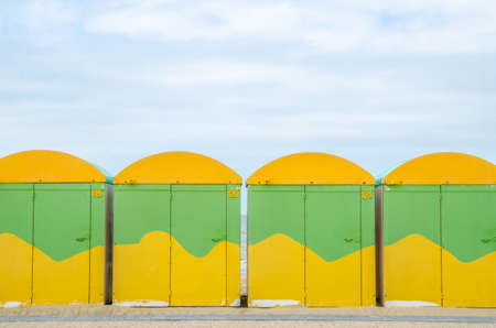 series of colourful costumes lined symmetrically on a beach with blue sky, clouds, sand on a sunny summer dayの写真素材