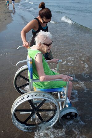 senior woman on a whellchair and beautiful mature caregiver by the seaの写真素材