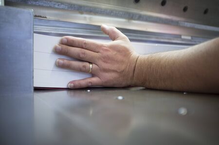 hand pushing a ream of paper on a industrial knife cutter