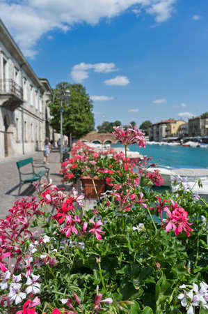 10, July, 2019 - Peschiera del Garda, Italy: The beautiful historical city center. Promenade and entertainment along the water canal, with colorful flowers, buildings and boatsのeditorial素材