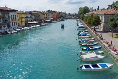 10, July, 2019 - Peschiera del Garda, Italy: The beautiful historical city center. Promenade and entertainment along the water canal, with colorful flowers, buildings and boatsのeditorial素材