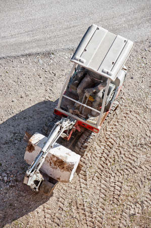 mini excavator, seen from above, working on dusty ground moves a large stone