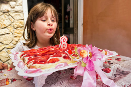 Young girl blowing out candles on eighth birthday strawberry cake