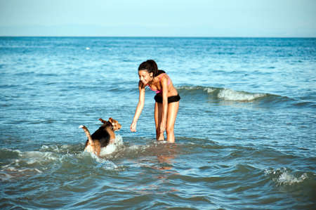 Happy girl with afro hairstyle, playing with a dog on the beachの写真素材