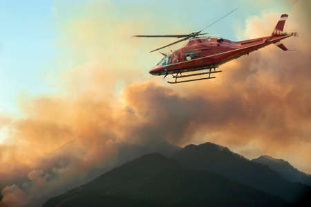 Firefighters helicopter monitor the fire in the mountain at sunset