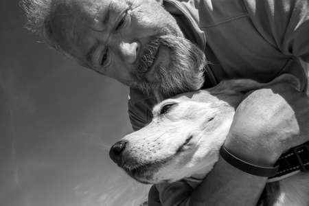 Mature man with beard hugging his old Beagle dogの写真素材