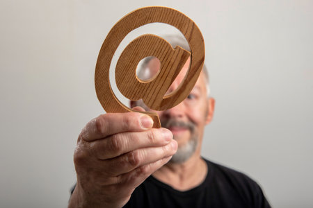 middle-aged man with in hand real email symbol carved in wood, in gray backgroundの写真素材