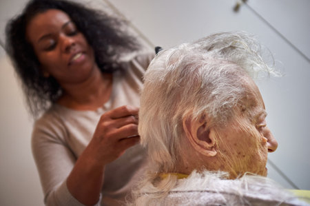 Caring African American woman caregiver, cutting her elderly woman hair at homeの写真素材