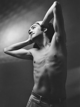 Black and white portrait of a young boy with long hair, hands on the head, and bare torsoの写真素材