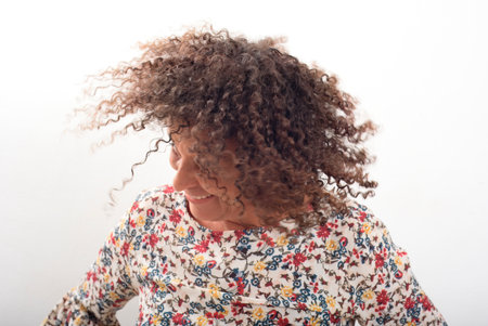 Joyful woman with curly hair captured in motion while smiling, wearing a colorful floral blouse against a white background. Concept of happiness, energy, freedom, and natural beauty. Perfect for lifestyle, diversity, and positive emotion themes.の写真素材