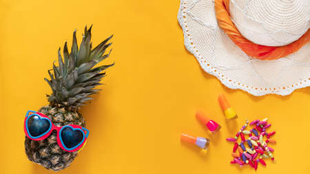 Summer composition. Pineapple in sunglasses, hat, beads and nail polishes on a yellow background with copy space. Vacation concept. Top view, flat lay.の写真素材