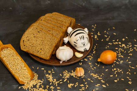 Sliced rye bread on a clay plate with garlic, onion and salt shaker in the shape of a cat.