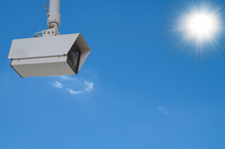 CCTV security camera against blue sky and sunの写真素材