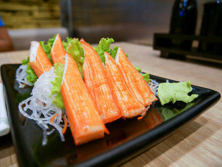 Crab stick in dark plate on wooden tableの写真素材