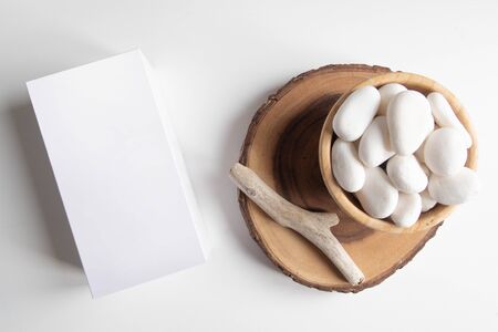 Mock up of white box and bowl with white pebble and wooden rustic sticks on white table. Boho design...