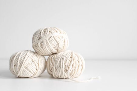 Balls of white yarn on a white wall background. Threads of wool boho image. Space for text. Good for macrame and handicrafts banners and promotionの写真素材