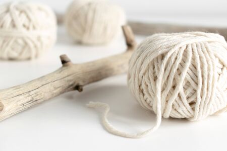 Balls of white yarn and rustic sticks on white table. Threads of wool boho image.Good for macrame...