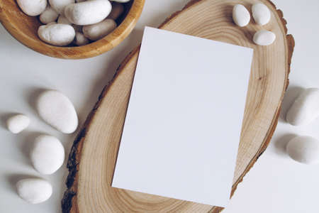 Boho vertical postcard mockup with white pebble and wooden cut section on white table background. Rustic bohemian image. Space for text. Good for handicrafts banners. Copyspace mockupの写真素材