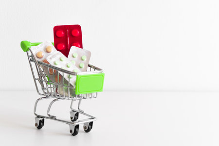 Shopping cart full of pills and medical drugs on white background. Small miniature shop trolley with space for your text. Copyspace pharmacy mockup bannerの写真素材