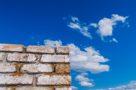 Old brick textured wall on the blue cloudy sky background. Fried orange moss on the white wall stock photo background. Copyspace for your text. Stock photoの写真素材