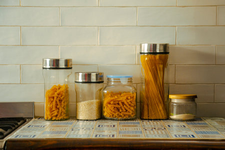 Various types of pasta in glass jars on the table in the kitchenの写真素材