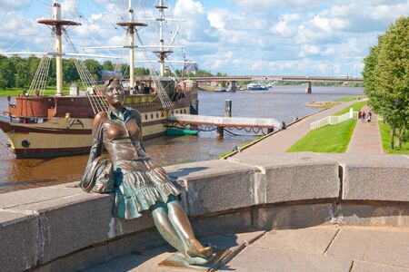 VELIKY NOVGOROD, RUSSIA - JULY 17, 2012. Sculpture of tired tourist girl. On the background is Volkhov River and sailing ship Restaurant Fregat Flagmanのeditorial素材