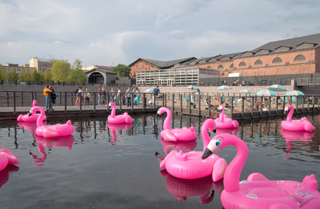 SAINT-PETERSBURG, RUSSIA - JUNE 11, 2018: New Holland Island. People rest on the sand beach in the center of the pond. Near the people are inflatable rubber pink flamingosのeditorial素材