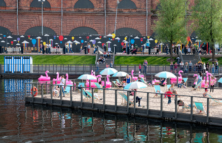 SAINT-PETERSBURG, RUSSIA - JUNE 11, 2018: New Holland Island. People rest on the sand beach in the center of the pond. Near the people are inflatable rubber pink flamingosのeditorial素材