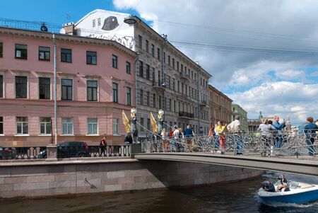 SAINT-PETERSBURG, RUSSIA - JULY 7, 2019: Many people take pictures on Bank Bridge with gilded wings of griffin statues. Excursion boat sailing Griboyedov Canalのeditorial素材