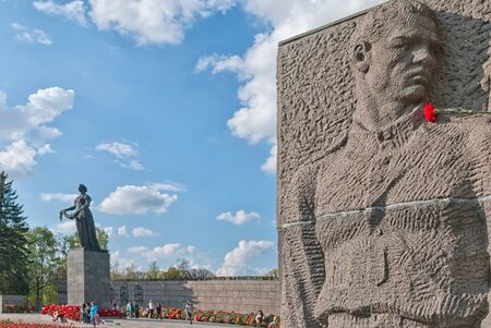 Saint-Petersburg, RussiaâMay 12, 2019: The sculpture of a soldier on the wall stela on Piskaryovskoye Memorial Cemetery. On the left side is Mother Motherland Statueのeditorial素材