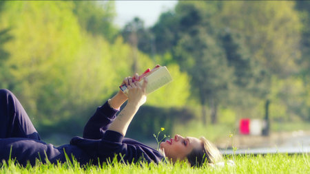 A Young Blond Woman is Relax and Reading Book on Grass in Natureの写真素材