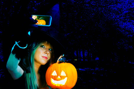 modern halloween witch with pumpkin takes a selfie photoの写真素材