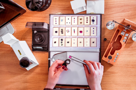 a gemologist examines a ruby using tweezers and evaluating gemstones - closeup view of gem specialists hands while at workの写真素材