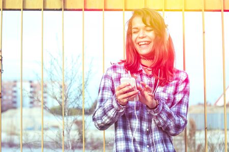 happy cheerful girl smiling listening to music with smartphone app outdoors - beautiful smile with bright teeth looking at the camera with bright eyes and laughing - concept of single woman and happinessの写真素材