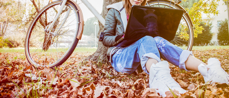 Urban girl with laptop in park. concept of eco-friendly lifestyle of freelance worker with bicycle remote working using communication and internet technology sitting in a quiet garden away  from the buzzling cityの写真素材