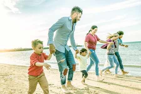 active family with many kids and friends on beach running together on the seashore. happy families of friends gettogether in summer beach holiday concept.の写真素材
