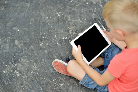 Teenage boy using a digital tablet in the street. Young boy sitting on the street.