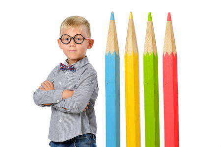 Serious boy in glasses and bowtie posing near huge colorful pencils. Educational concept. Isolated over white. School preschoolの写真素材